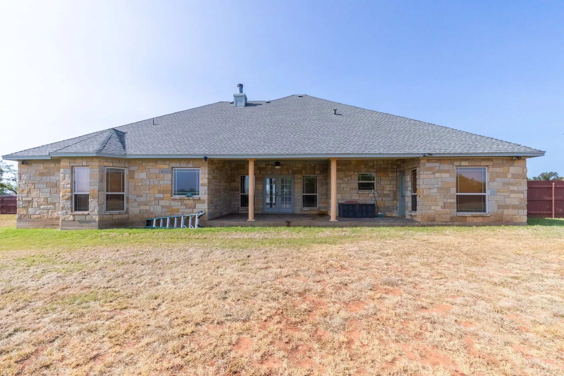 Rear exterior featuring stone veneer, a covered patio, and multiple windows