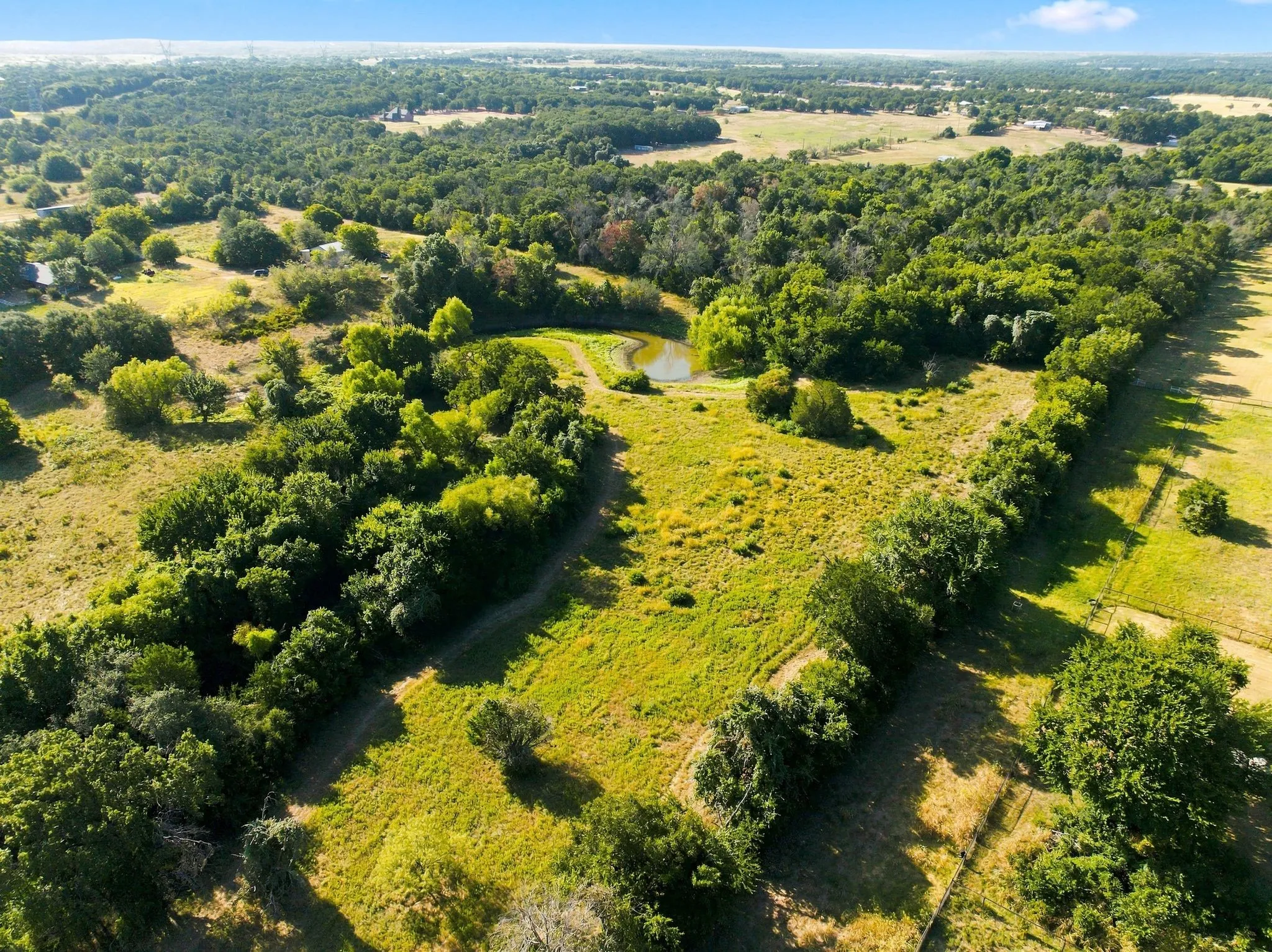Sprawling rural acreage featuring mature tree-lined boundaries, meandering waterway, and expansive pastureland with rolling topography