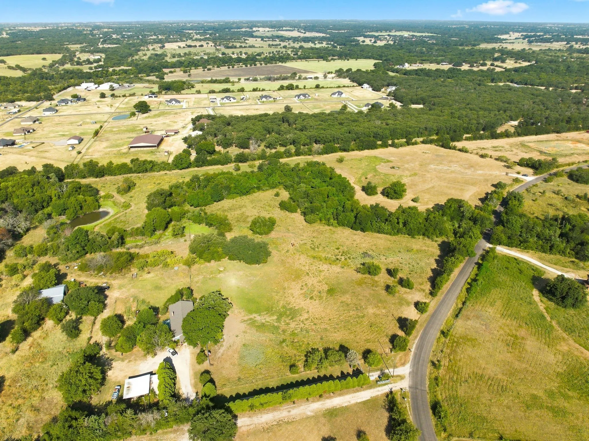 Expansive acreage with a winding paved road, scattered mature trees, and a visible pond