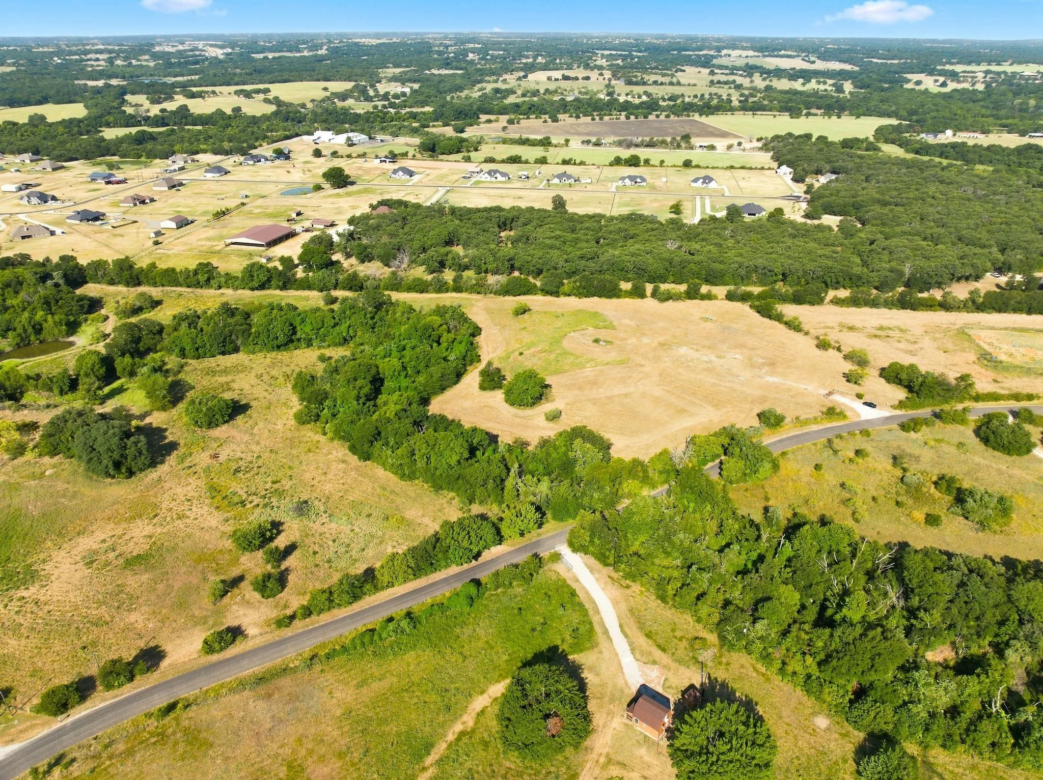 Expansive rural acreage featuring mature tree clusters, open pastureland, and a paved driveway with direct road access