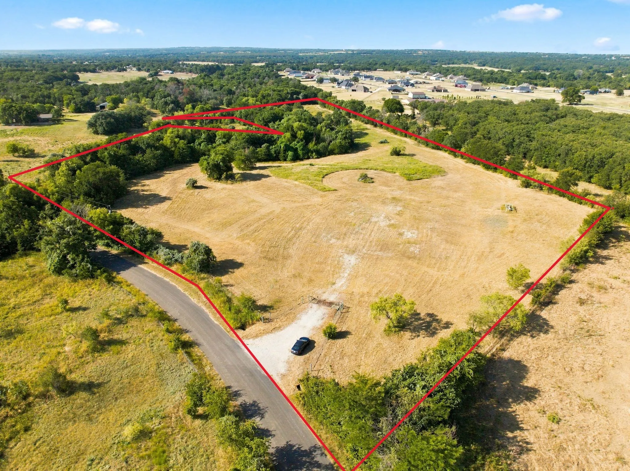 Expansive land parcel featuring open fields, mature trees, and a paved road access point