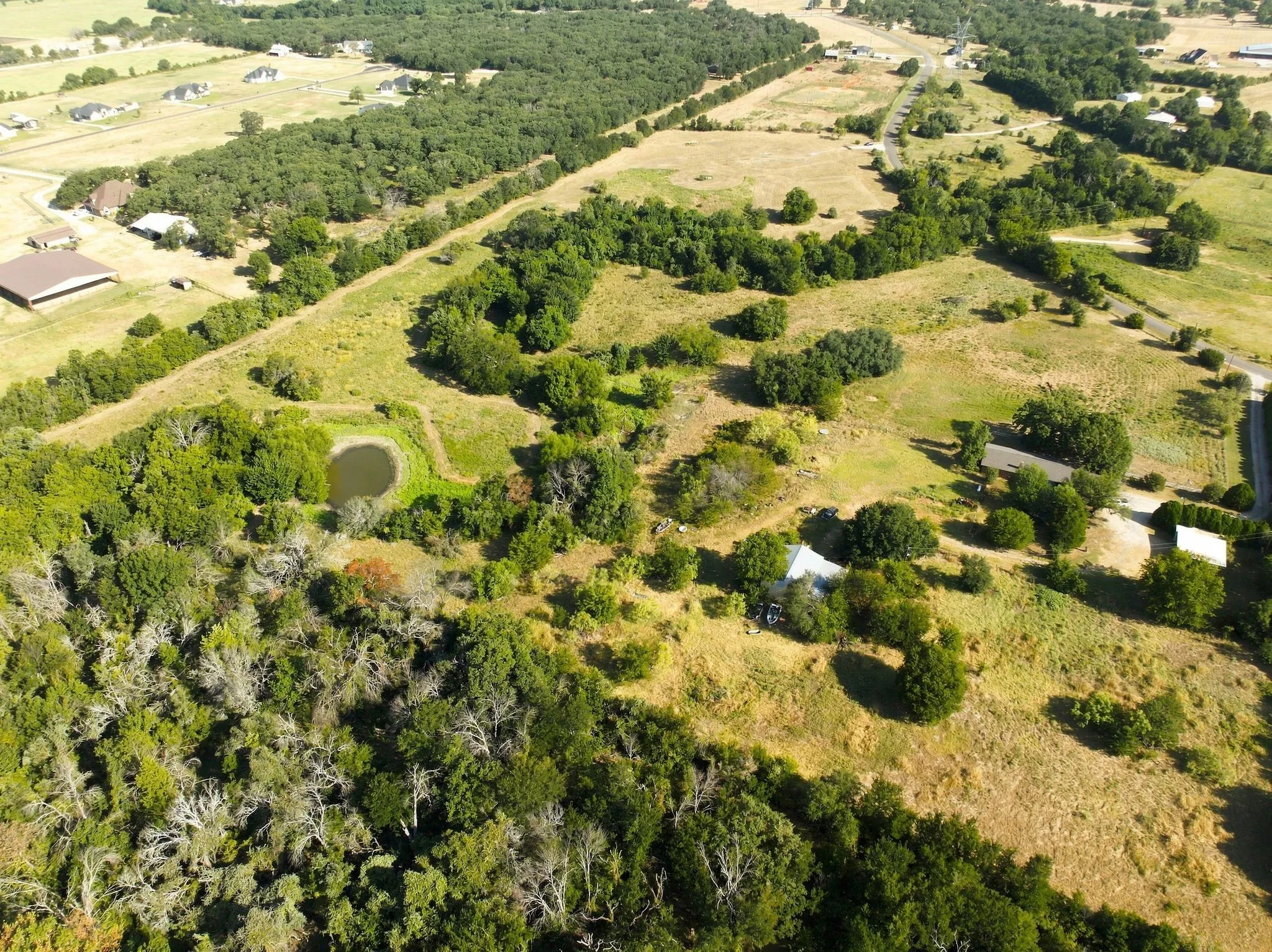 Expansive land parcel featuring open fields, wooded areas, and a visible pond