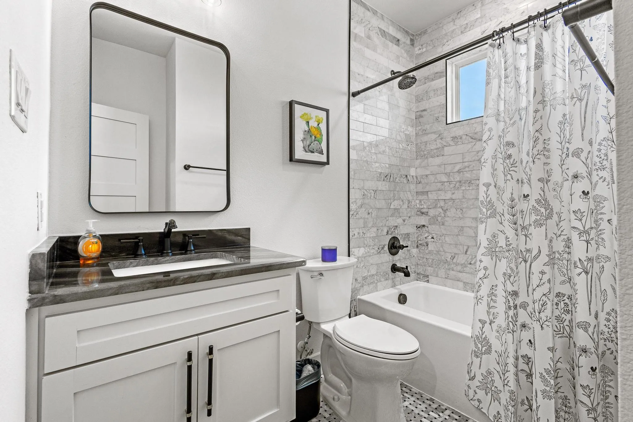 White vanity with black hardware, rectangular undermount sink, and a dark stone countertop