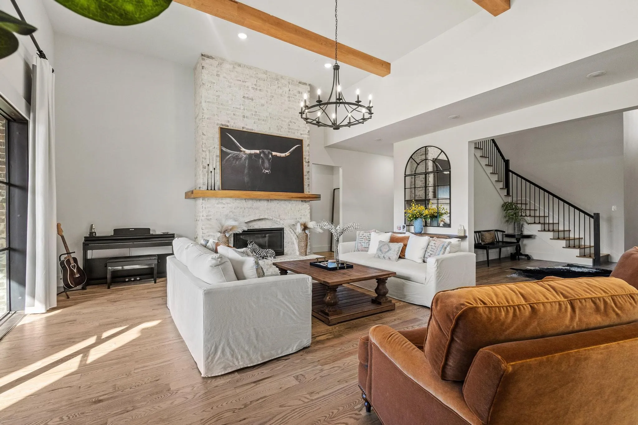 Spacious living area featuring a vaulted ceiling with exposed wood beams, a white brick fireplace, and wood-finish flooring