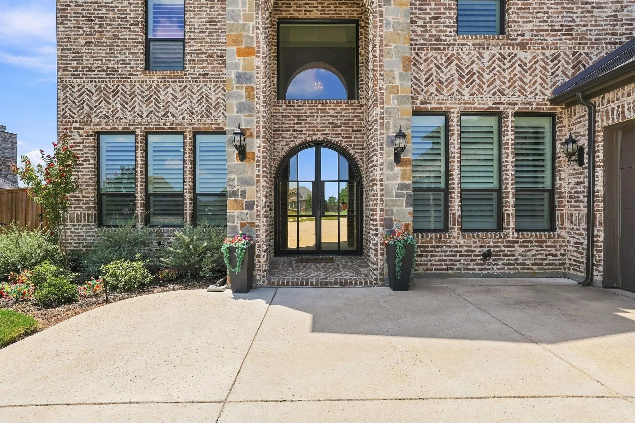 Brick and stone facade with arched entry, complementing windows, and integrated outdoor lighting