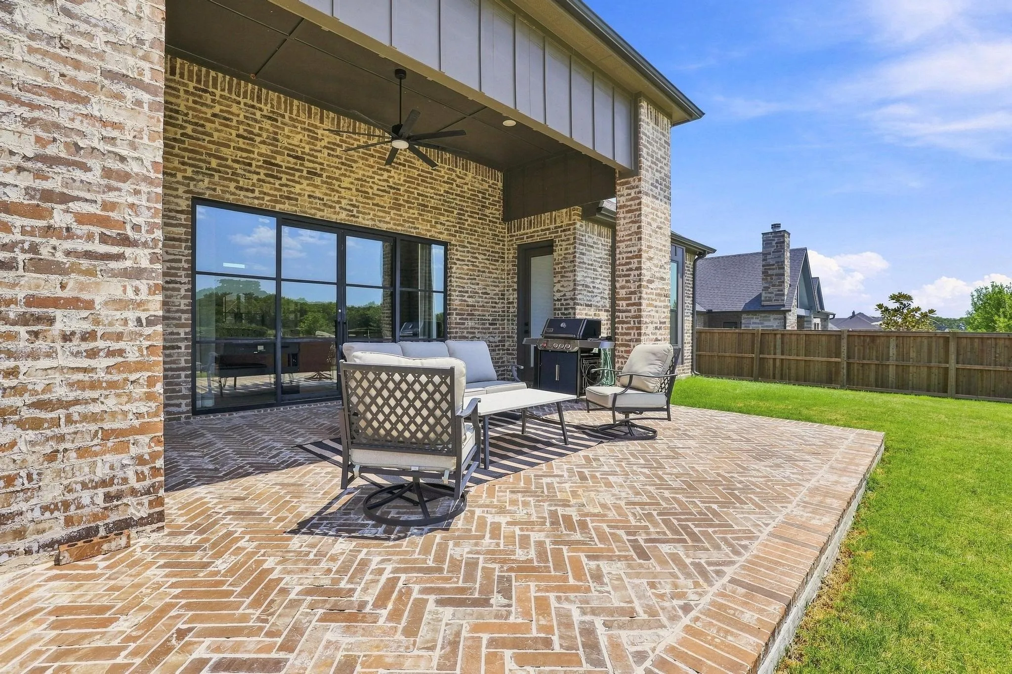 Covered patio featuring a herringbone brick pattern, a ceiling fan, and large black-framed glass doors