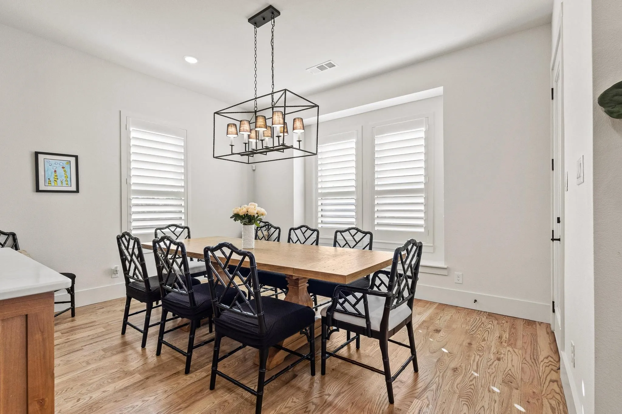 Dining area with hardwood flooring, a multi-paneled chandelier, and three windows featuring white louvered shutters