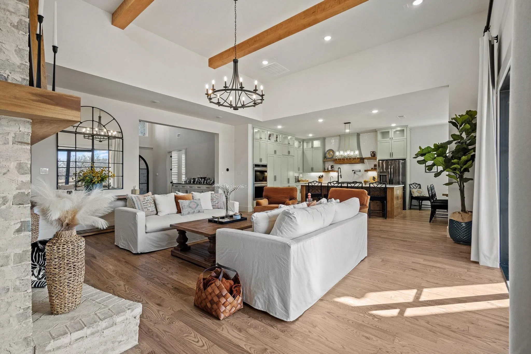 Spacious living area featuring high vaulted ceilings with exposed wood beams, a prominent stone fireplace with a wood mantel, and wood-finish flooring