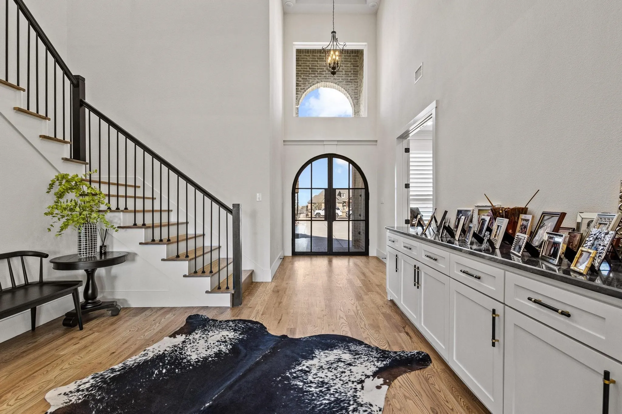 Double-height entryway featuring a decorative arched window, dark-framed arched glass entry doors, and light wood-finish flooring