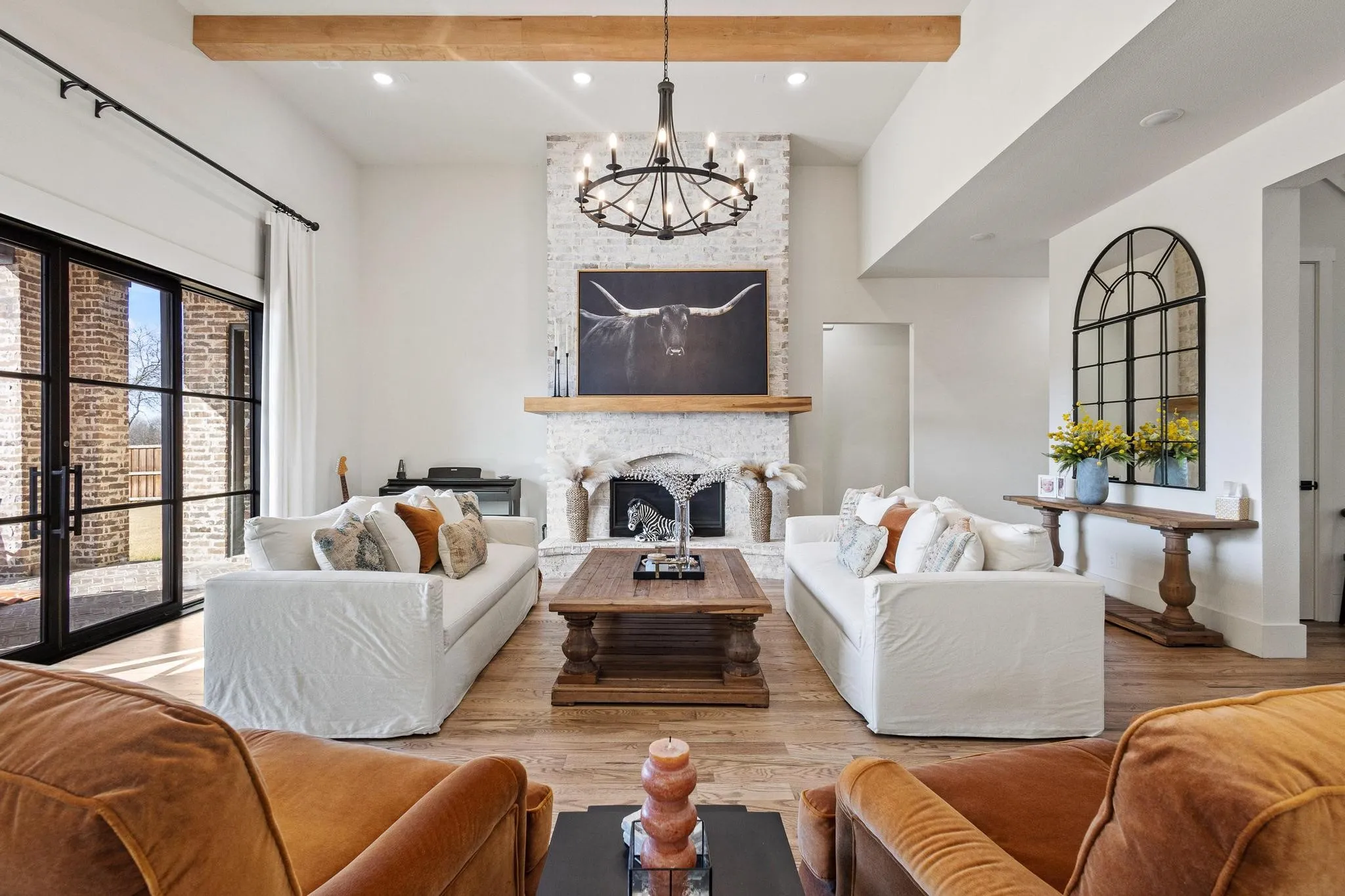 Spacious living area featuring a vaulted ceiling with exposed wood beams, a whitewashed brick fireplace with a wood mantel, and wood-finish flooring