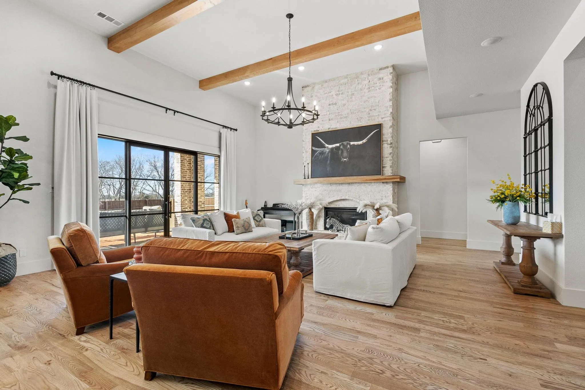Vaulted ceiling with exposed wood beams, a whitewashed brick fireplace with wood mantel, and wood-finish flooring