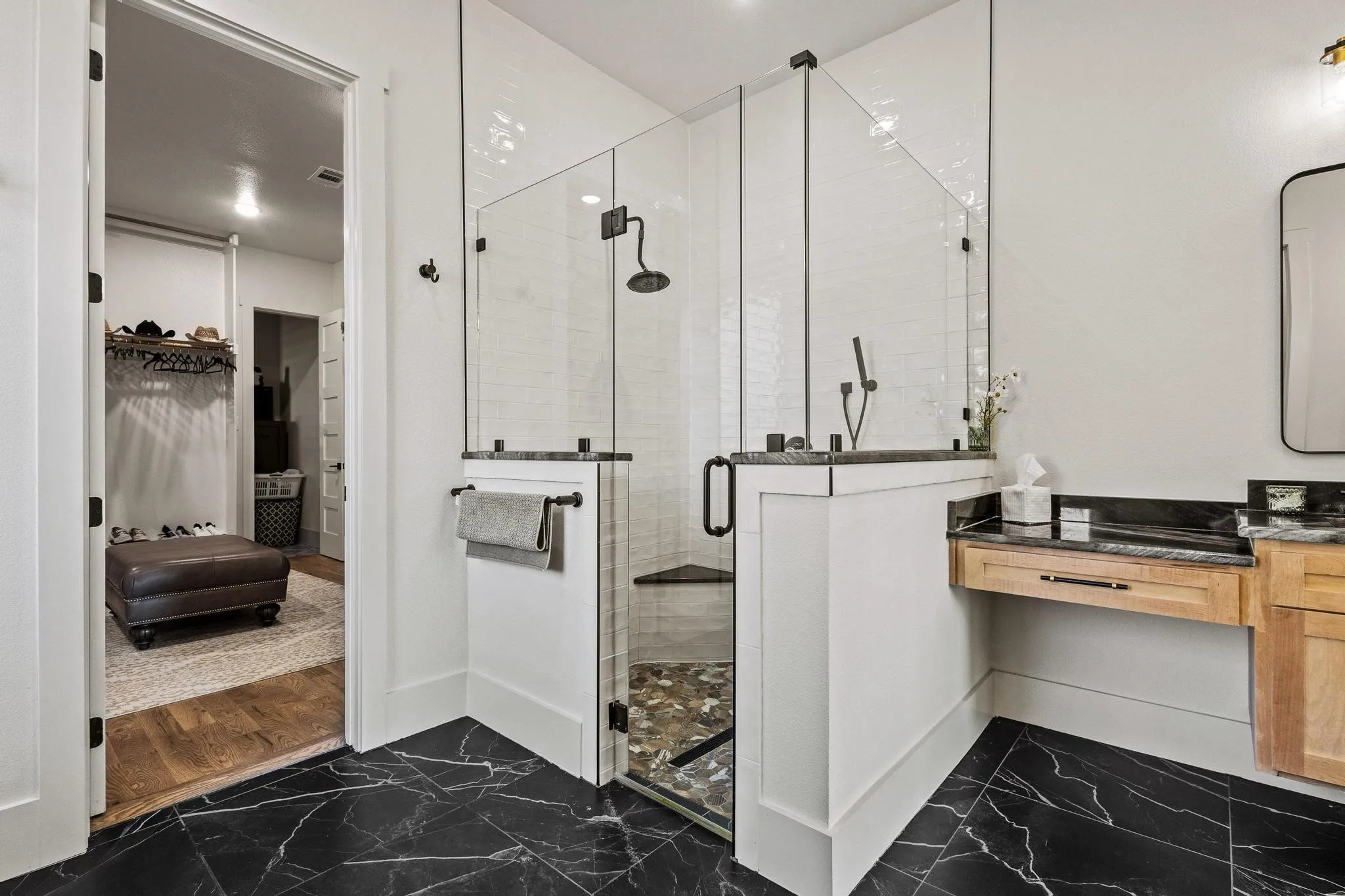 Black marble-look tile flooring grounds this bathroom featuring a glass-enclosed shower with dual showerheads