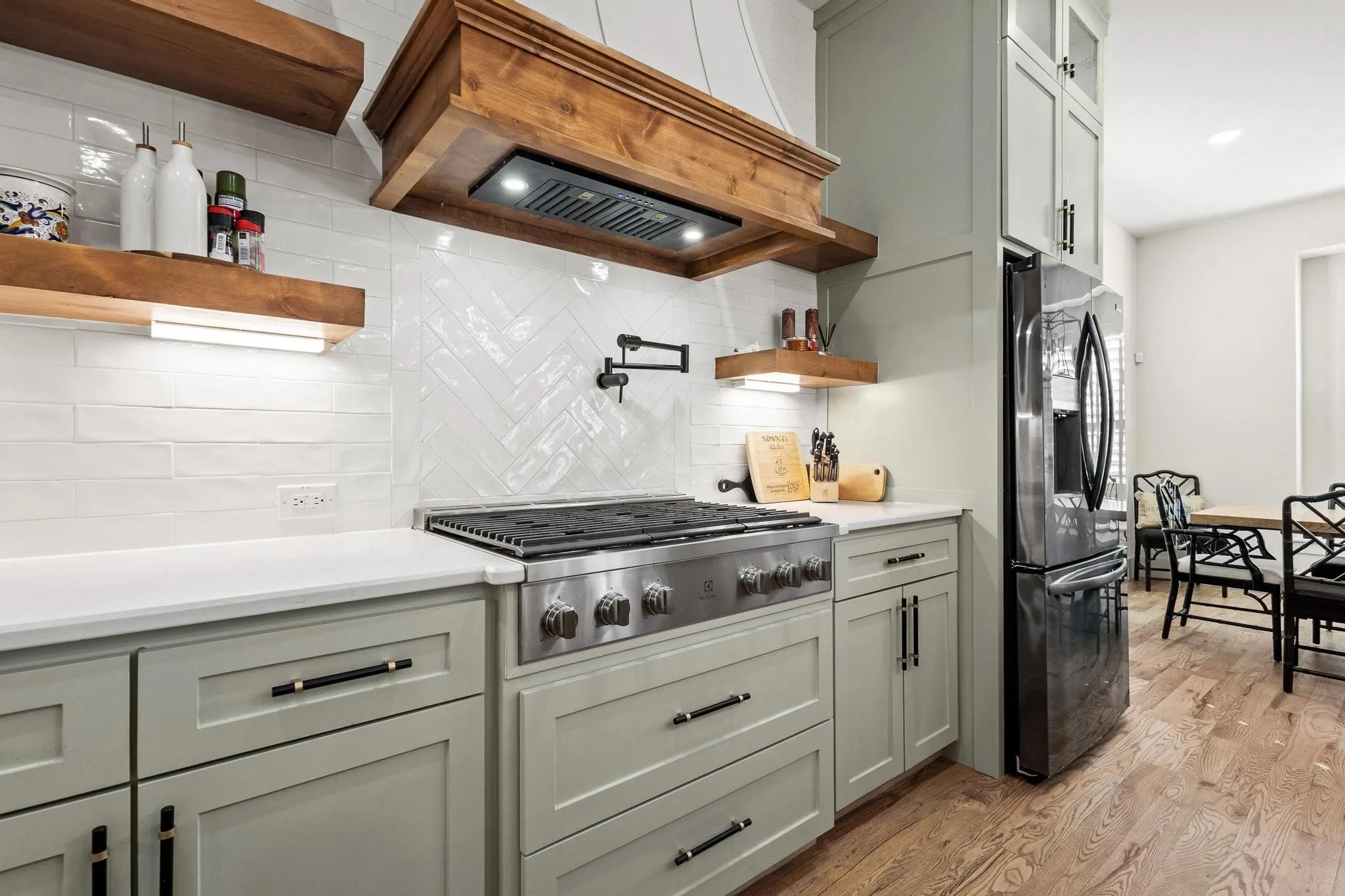 Gourmet kitchen featuring light green cabinetry, white countertops, stainless steel appliances, a herringbone tile backsplash, and wood-finish flooring