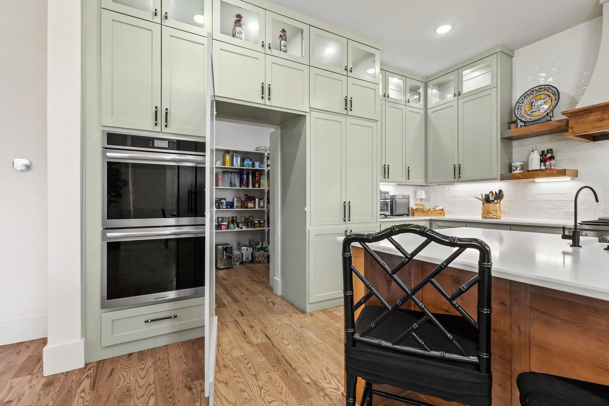 Kitchen featuring extensive light green cabinetry, stainless steel double wall ovens, wood-finish flooring, white countertops, and a full-height tile backsplash