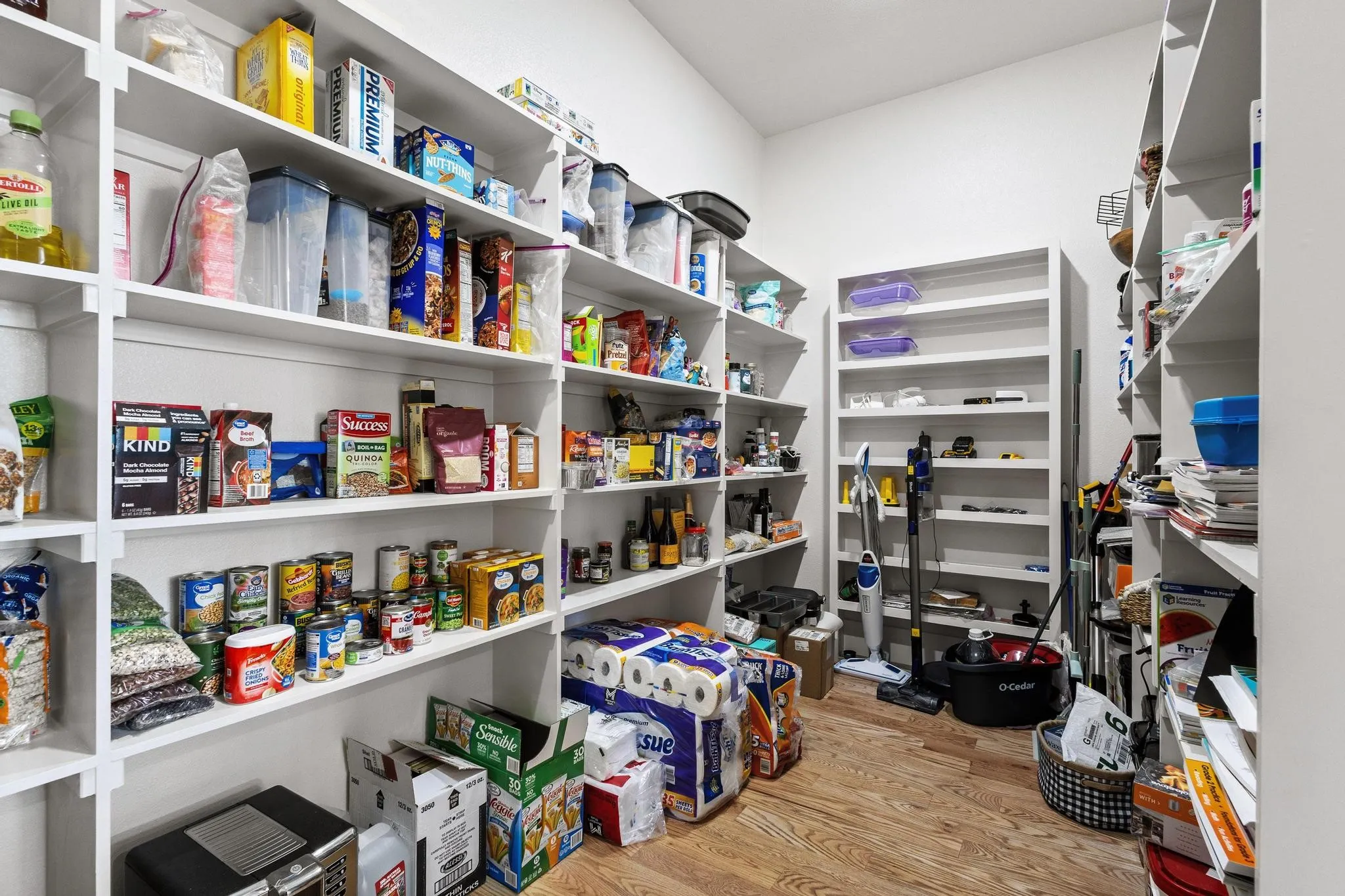 Walk-in pantry featuring extensive built-in shelving, white walls, and wood-finish flooring