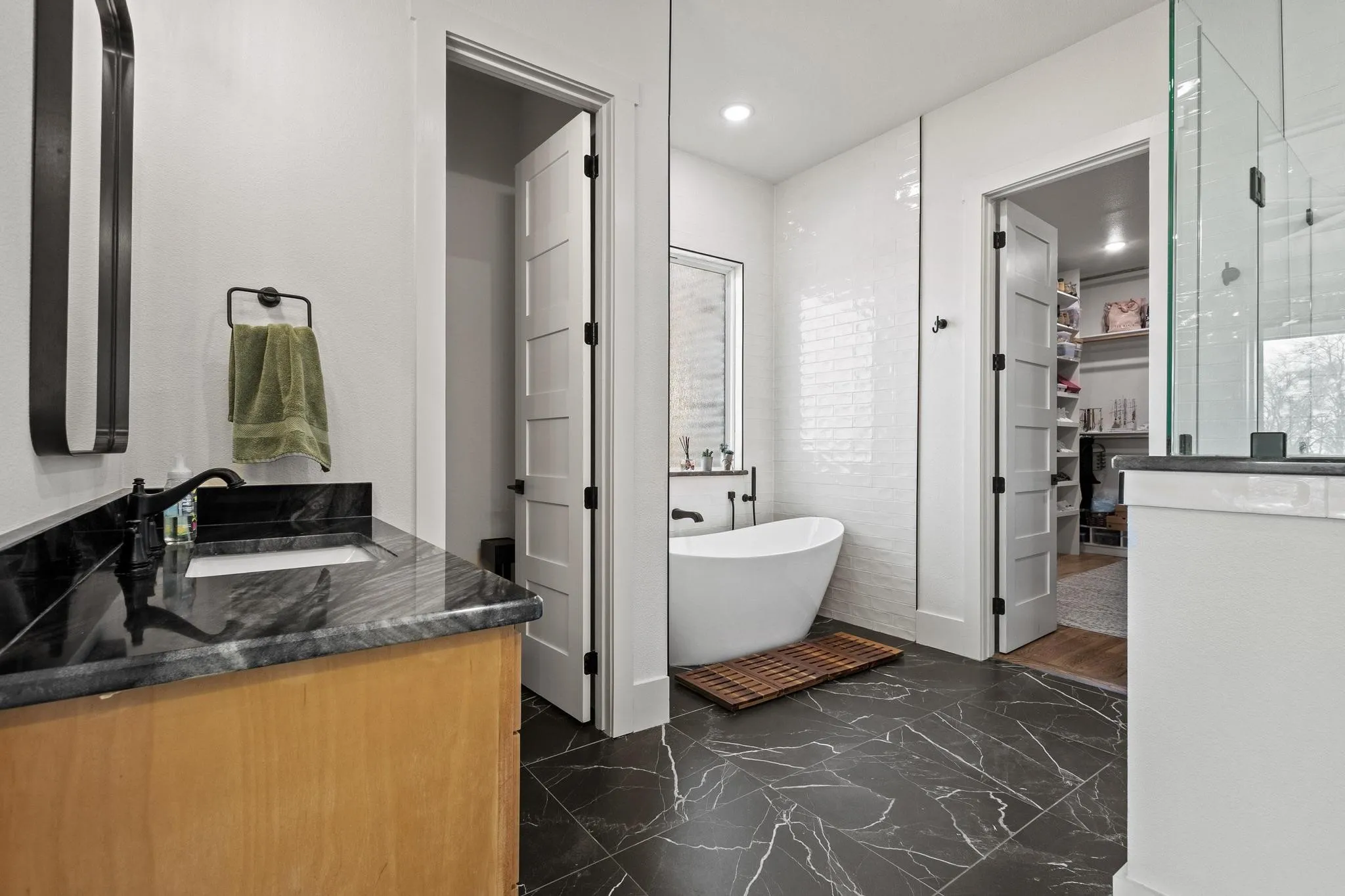 Spacious bathroom featuring a freestanding soaking tub, dark marble-look floor tiles, and a vanity with a dark countertop and undermount sink