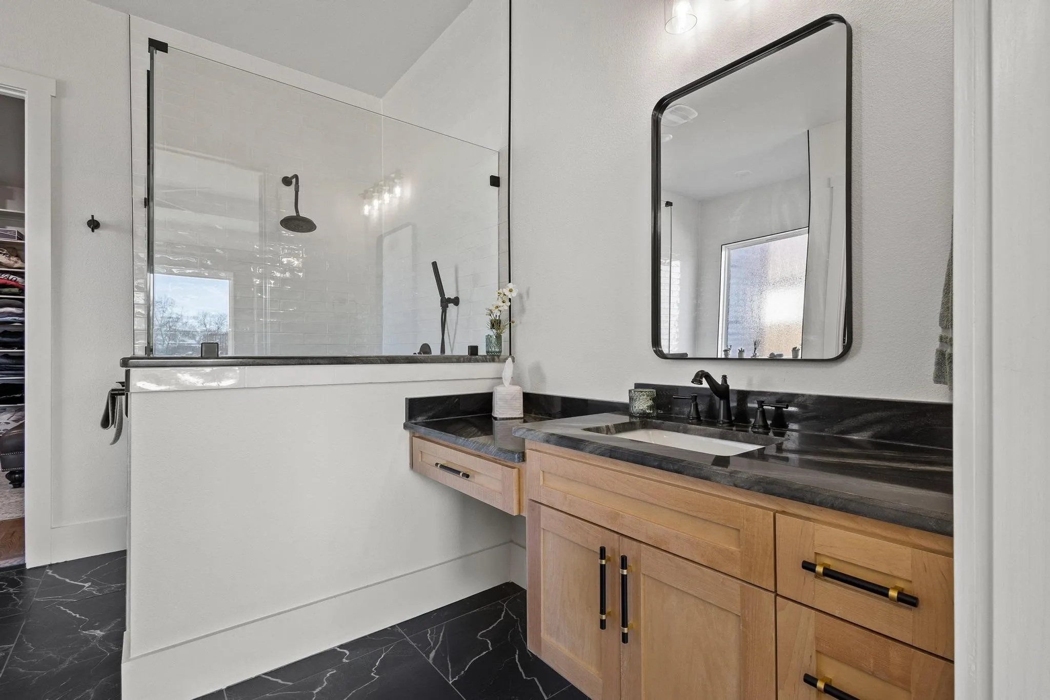 Bathroom featuring a wood-finish vanity with black countertop, under-mount sink, and matte black fixtures