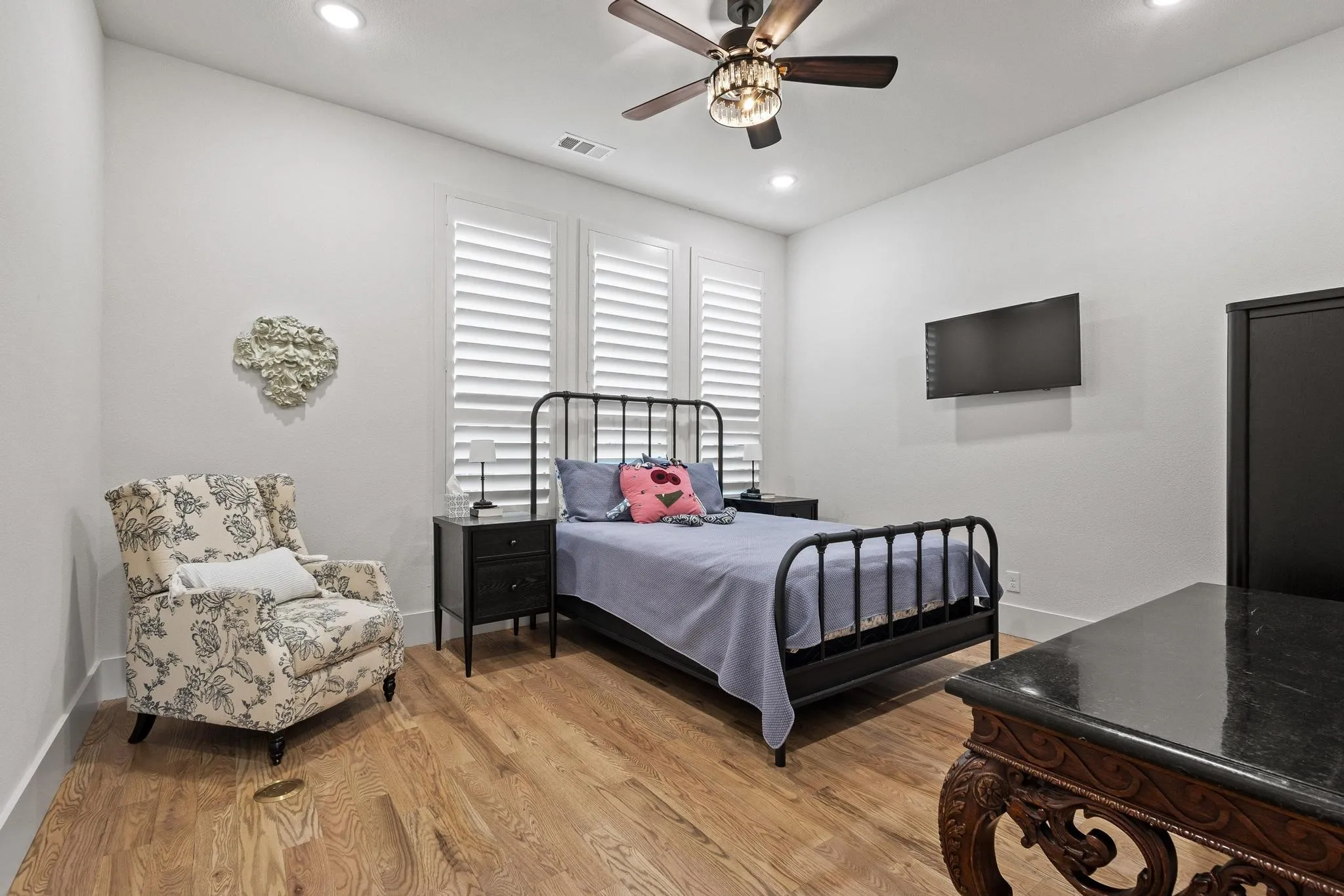 Wood-finish flooring throughout, featuring a ceiling fan with integrated lighting, recessed lighting, and white plantation shutters on multiple windows