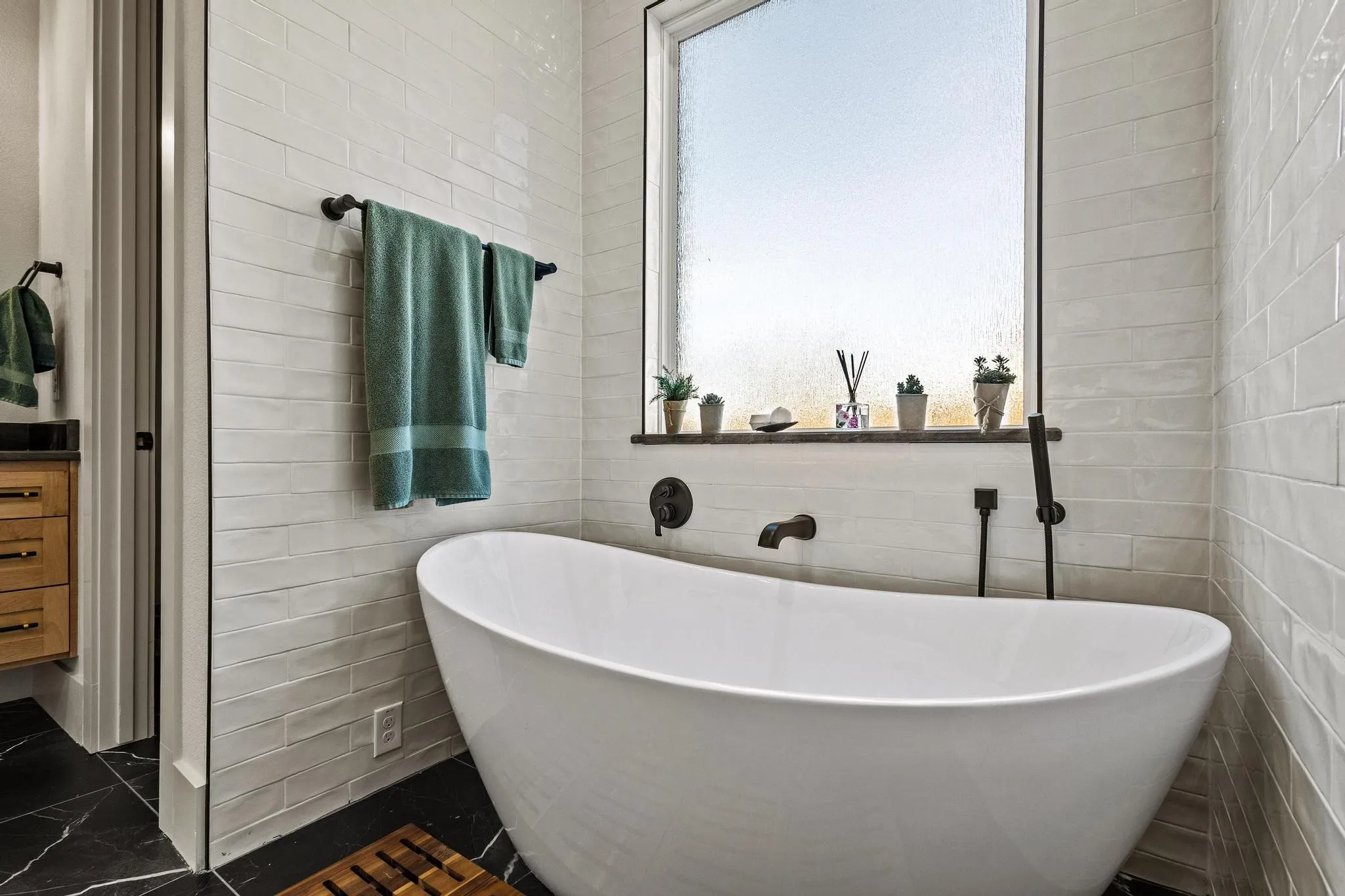 Freestanding soaking tub with matte black fixtures, set against a white subway tile wall