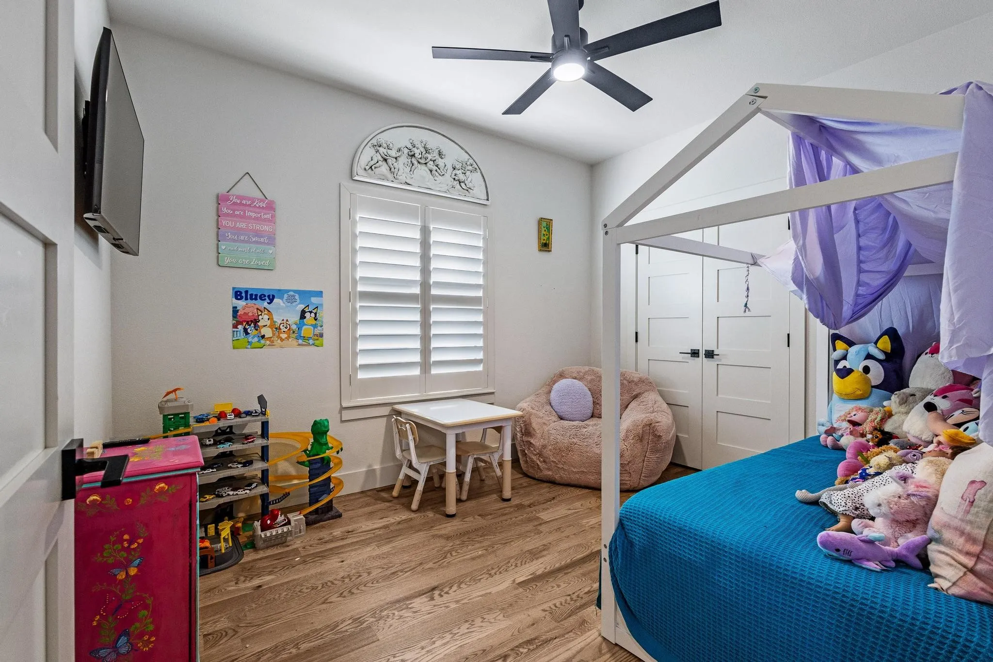 Vaulted ceiling room featuring wood-finish flooring, a ceiling fan, and white plantation shutters with an arched transom window