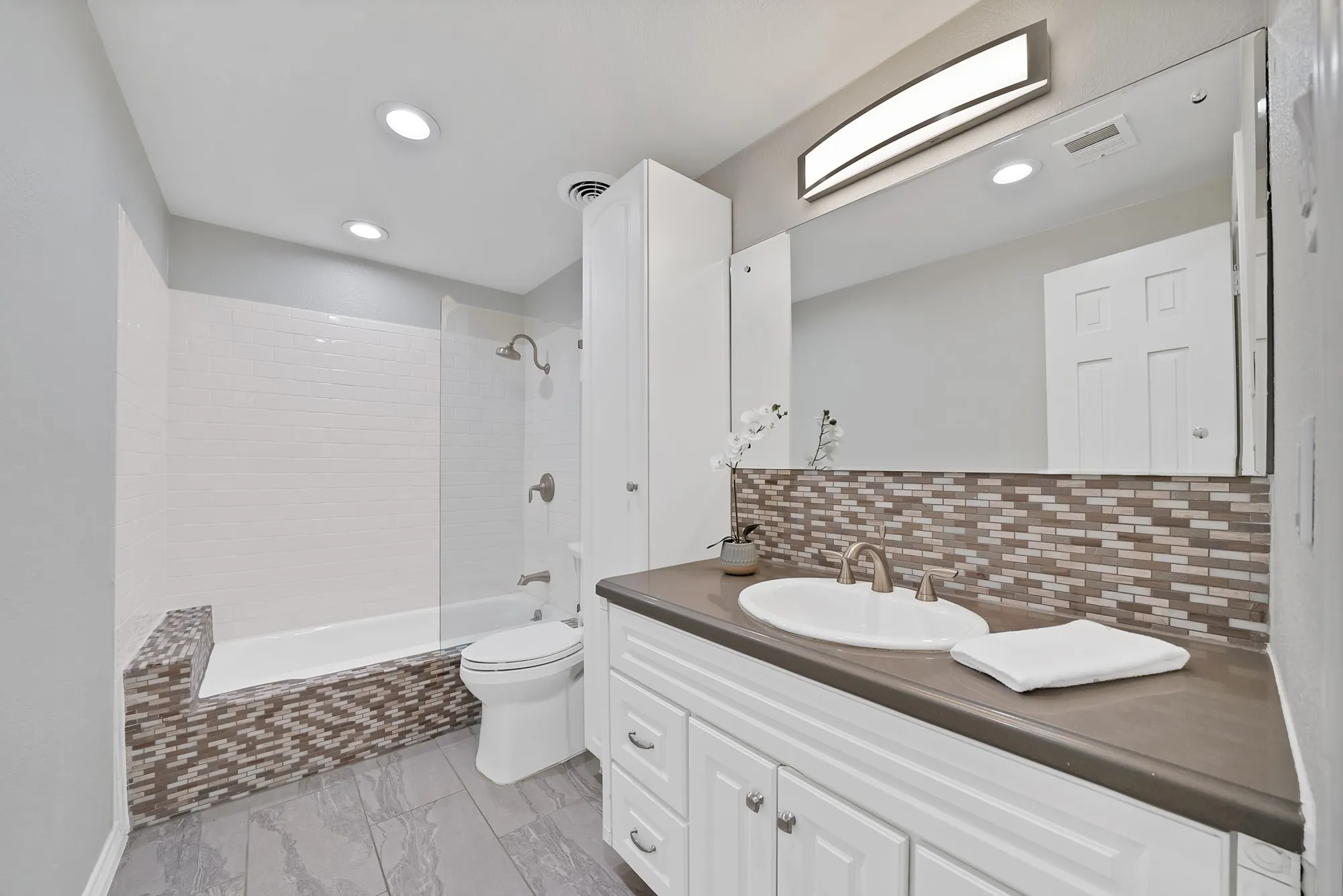 White vanity with integrated sink, rectangular mirror, and mosaic tile backsplash
