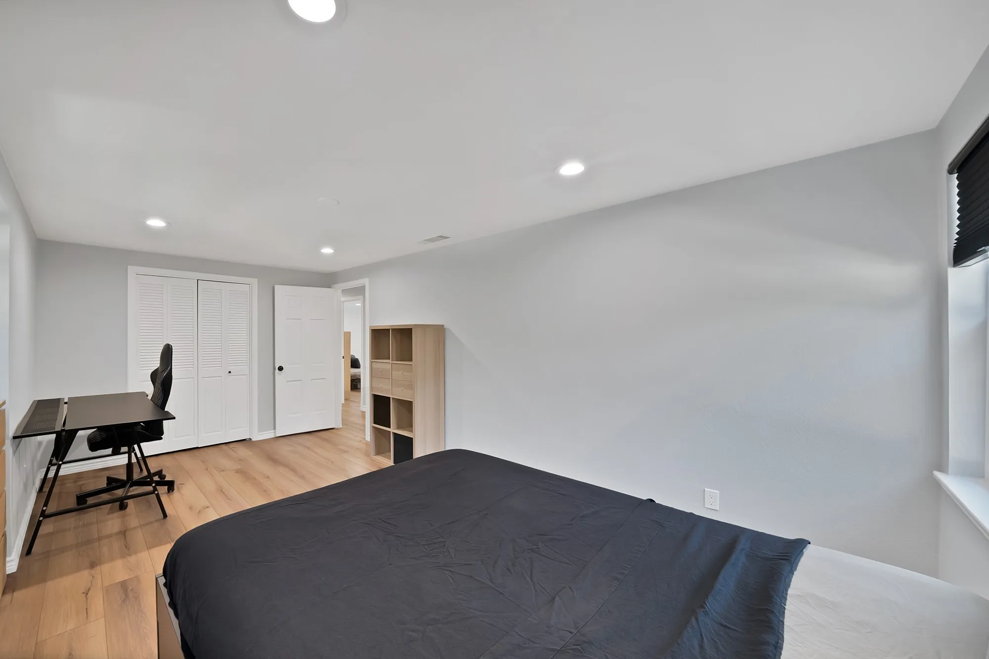Bright, versatile bedroom featuring recessed ceiling lighting, wood-finish flooring, and built-in shelving unit