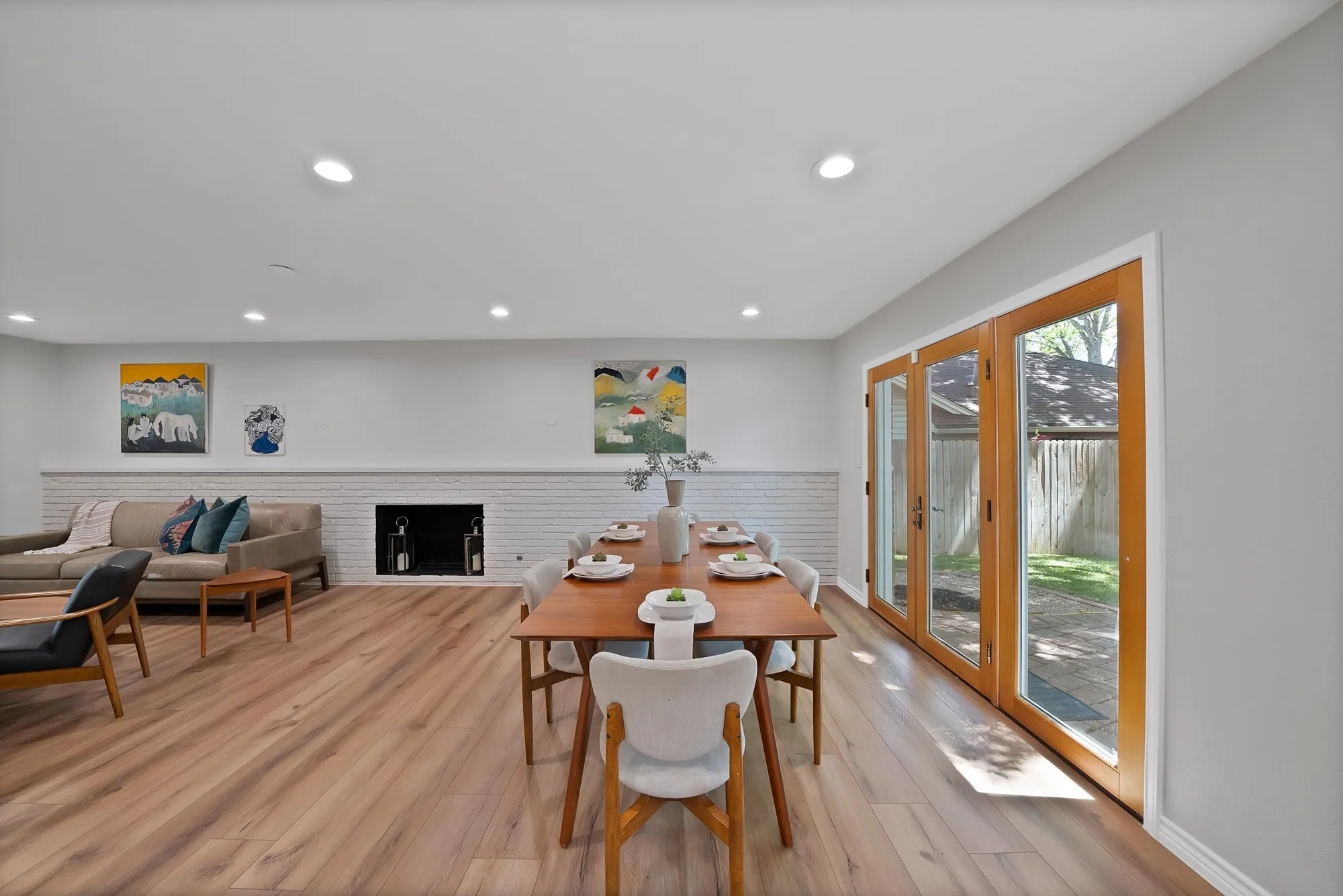 Recessed lighting, wood-finish flooring, white brick fireplace, light gray wall paint, and wood-frame glass doors