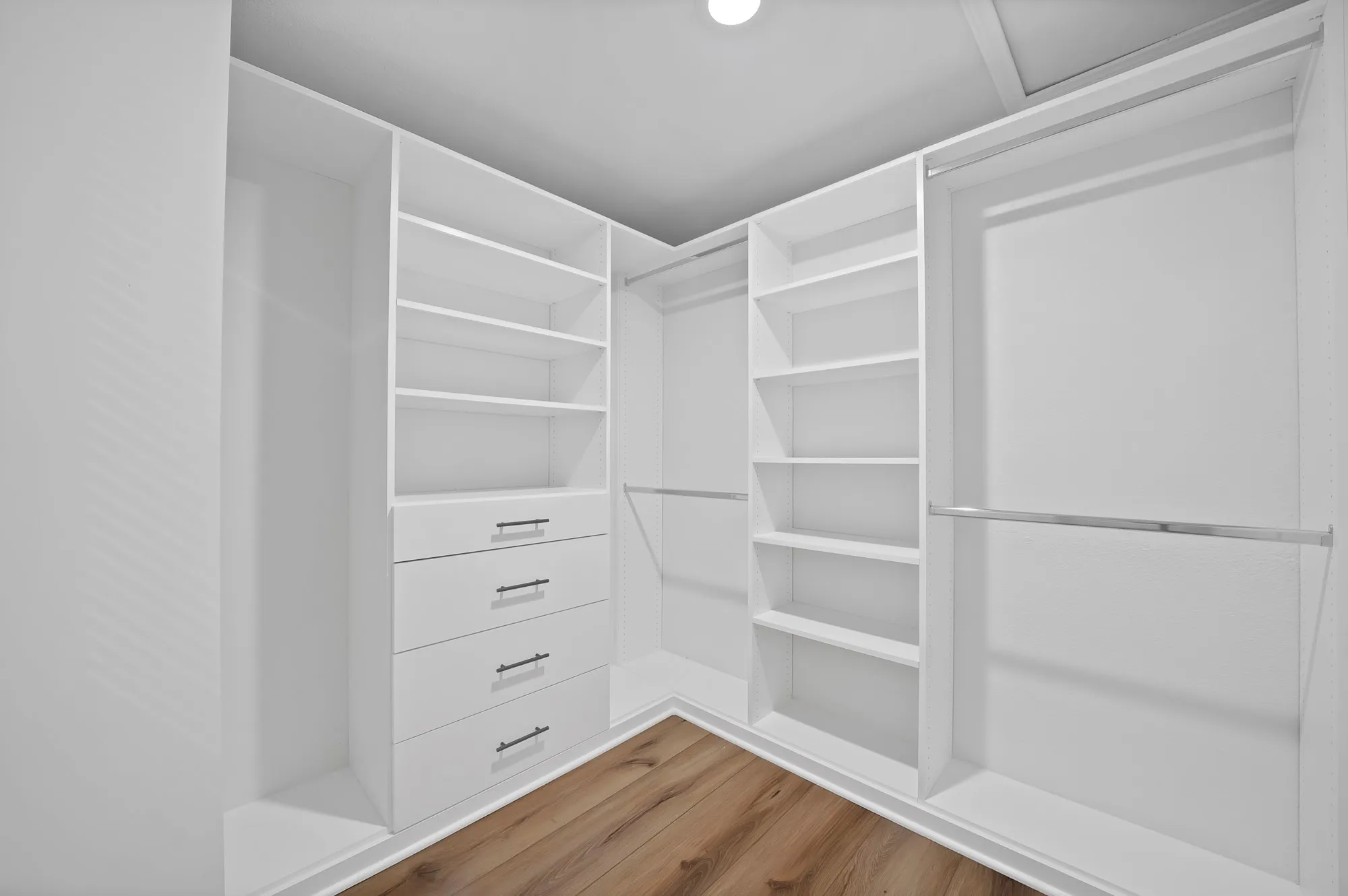 Custom closet system with white cabinetry, integrated shelving, pull-out drawers with dark hardware, and chrome hanging rods, all set against wood-finish flooring