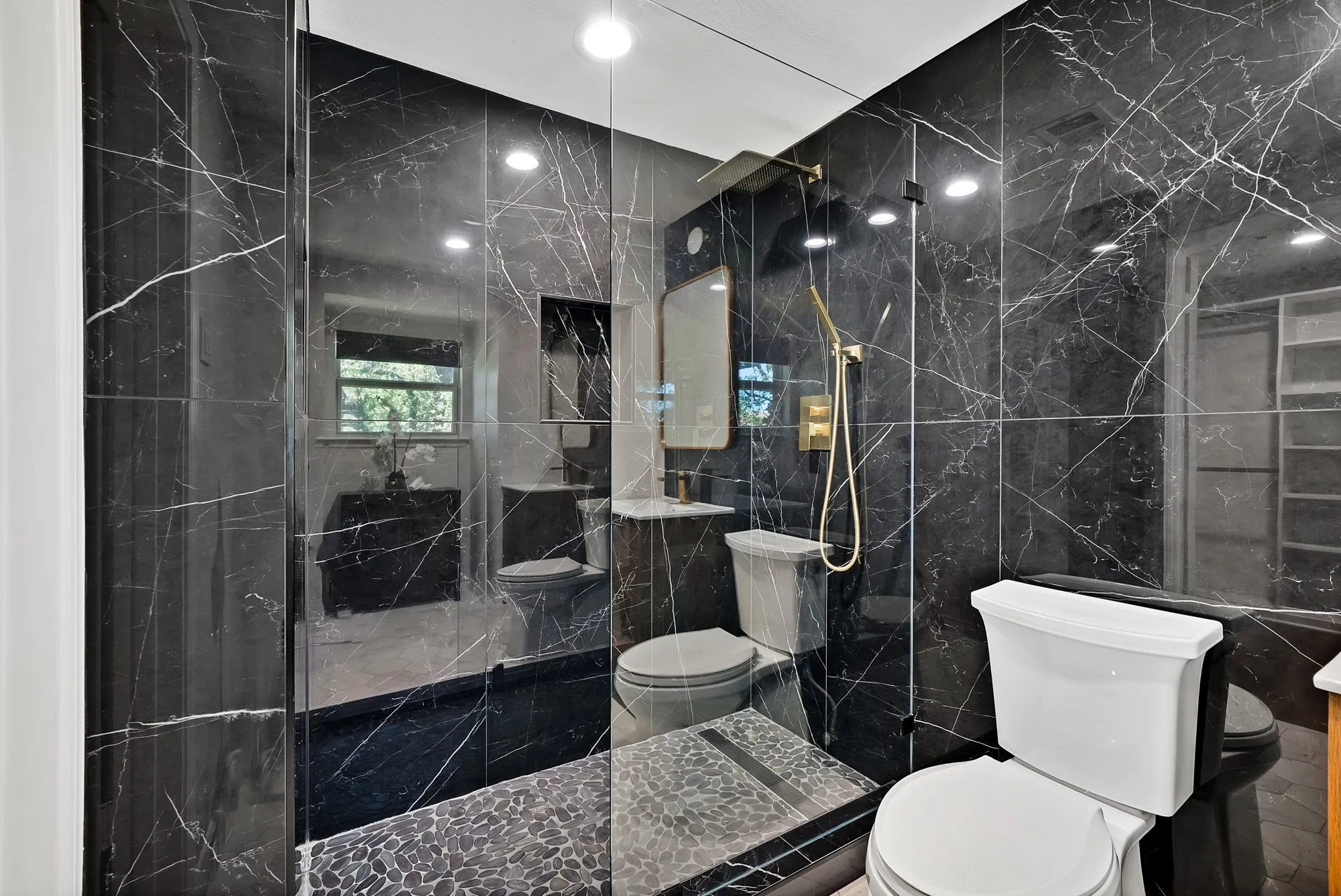 Luxurious primary bathroom featuring sleek black marble-look tile walls with white veining, a spacious walk-in shower with frameless glass enclosure and rainfall showerhead, dual vanity with vessel sink, and recessed ceiling lighting throughout