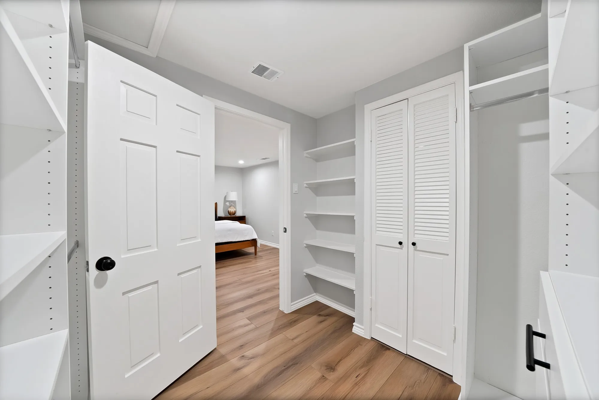 Walk-in closet featuring white built-in shelving, wood-finish flooring, and a six-panel door