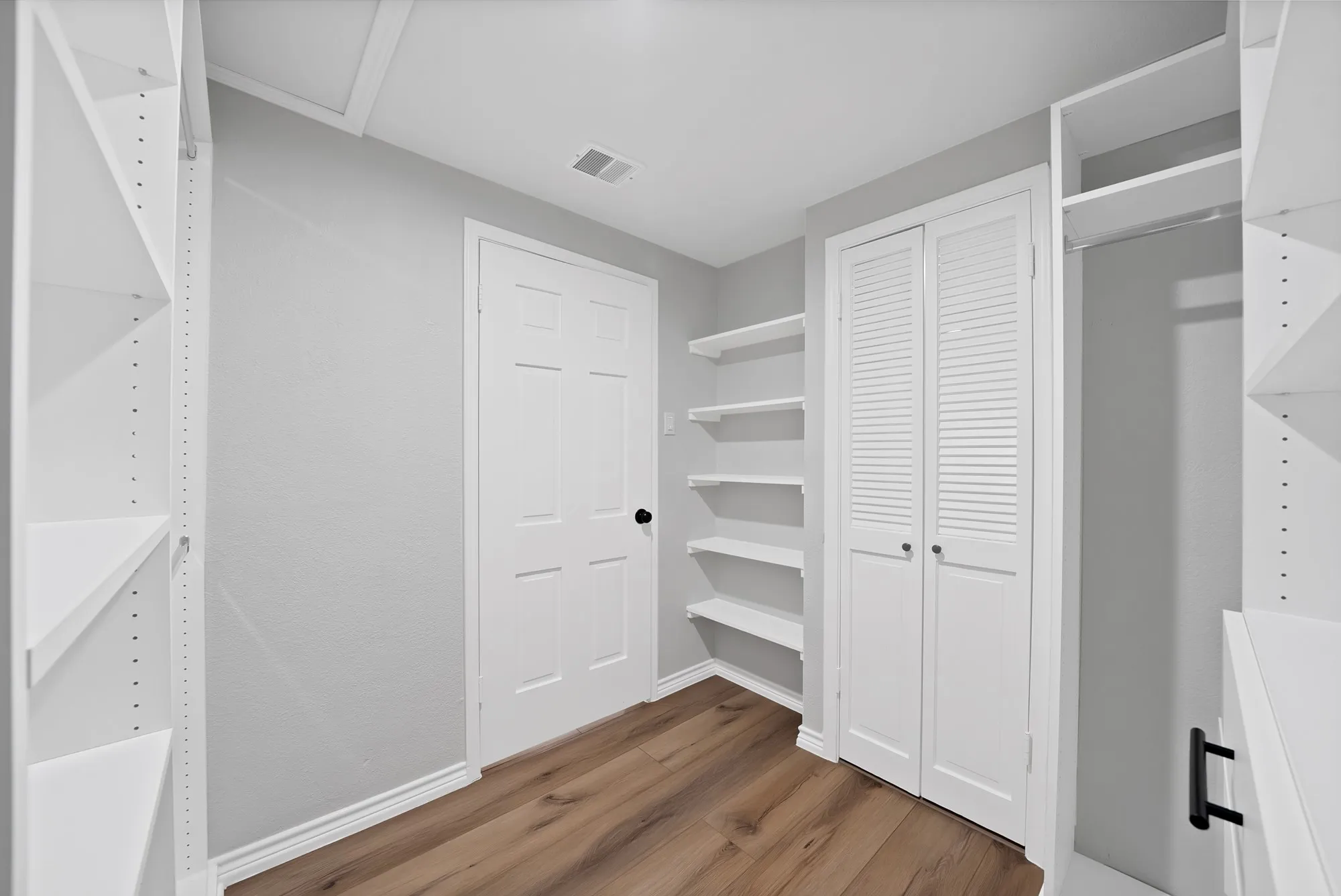 Spacious walk-in closet featuring wood-finish flooring, white built-in shelving, white bifold doors, and a clothing rod