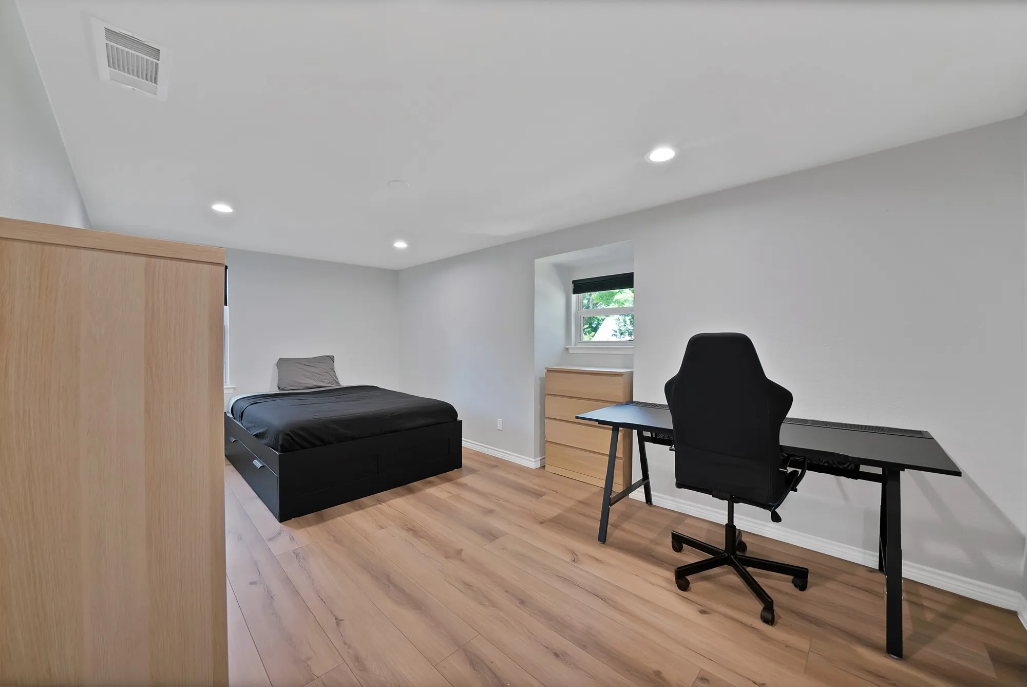 Versatile bedroom featuring warm wood-finish flooring, recessed ceiling lighting, and a large closet with wood-finish doors