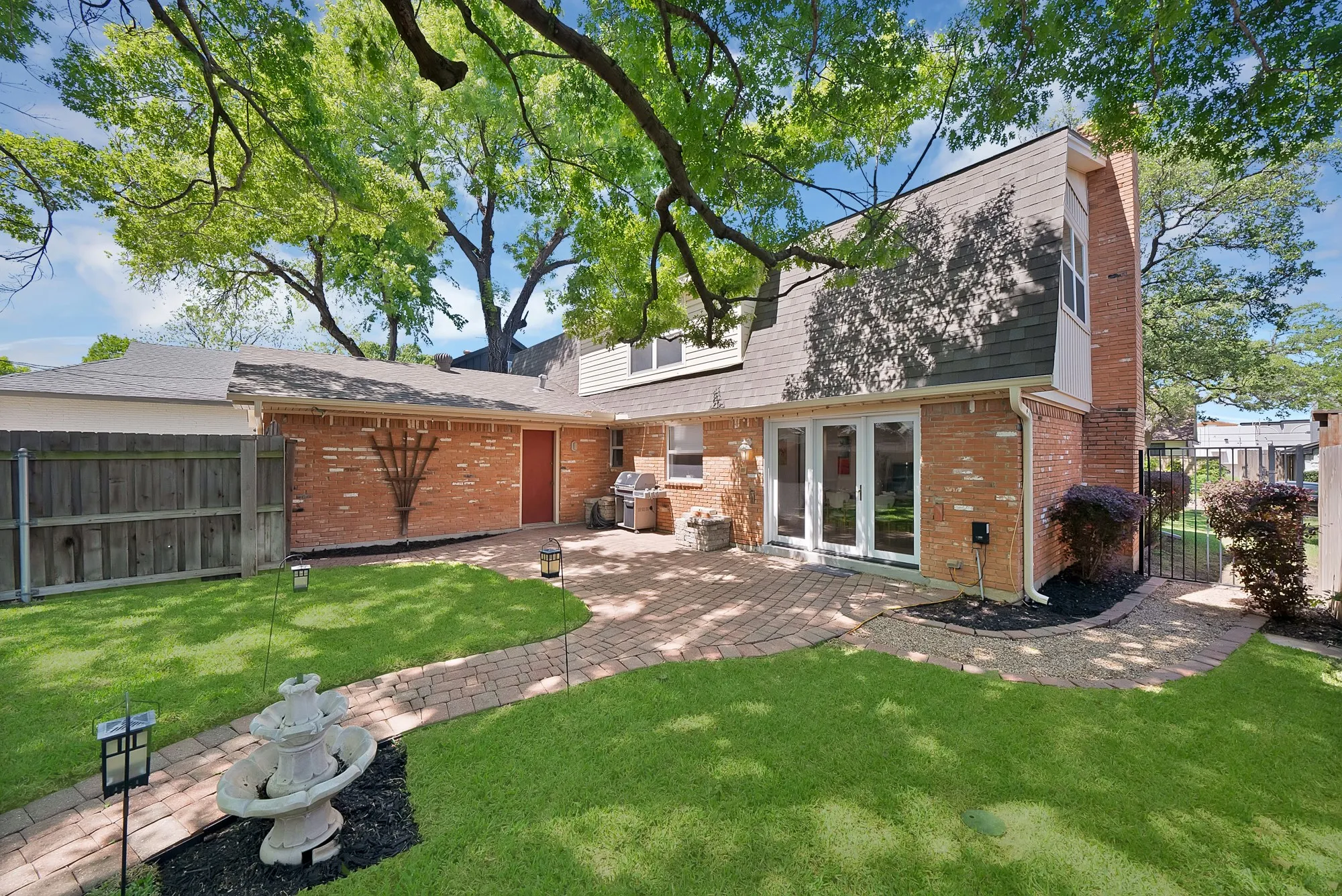 Expansive backyard featuring a brick patio, mature trees, and a privacy fence