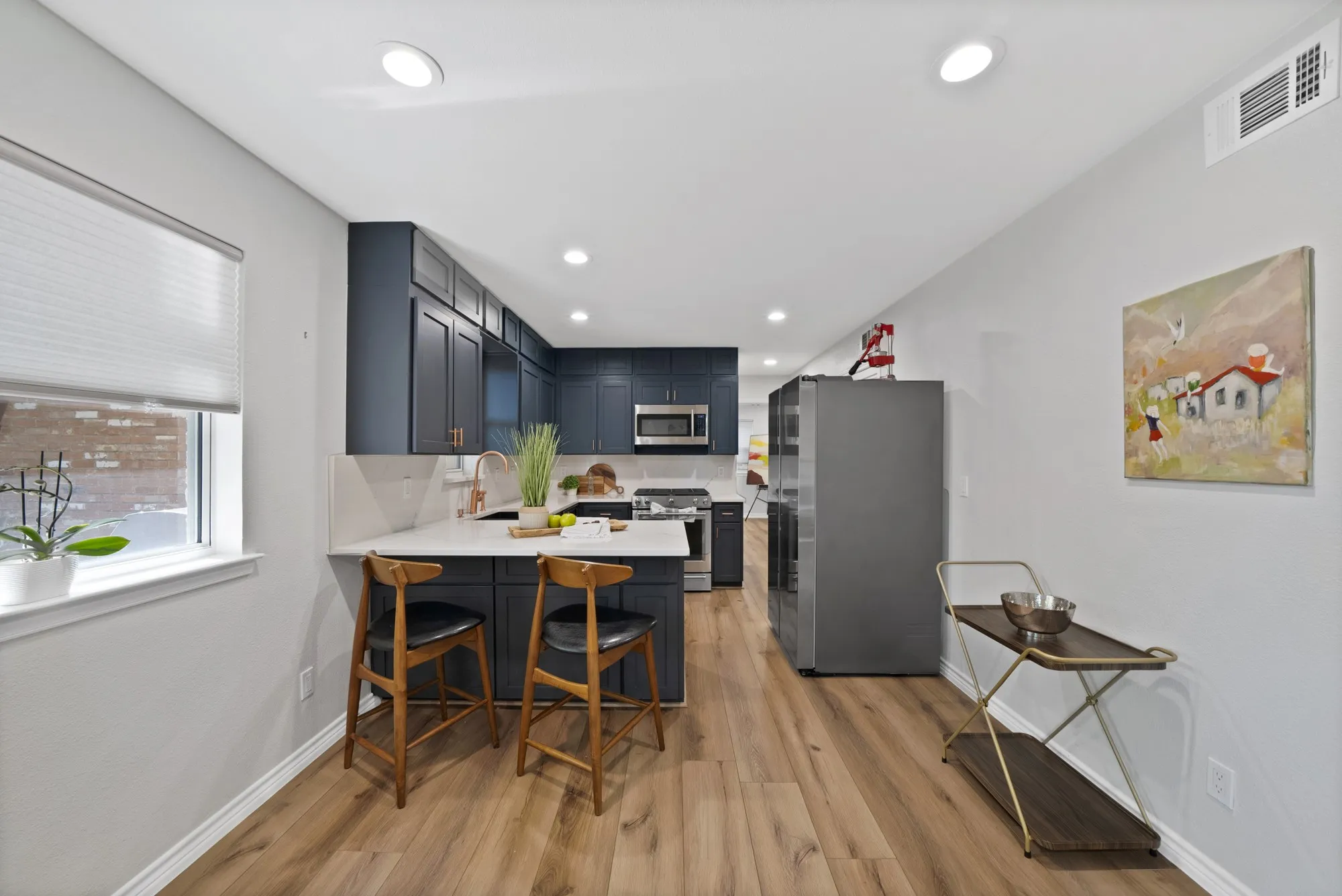 Modern kitchen featuring dark cabinetry, stainless steel appliances, light countertops, a kitchen island, and wood-finish flooring