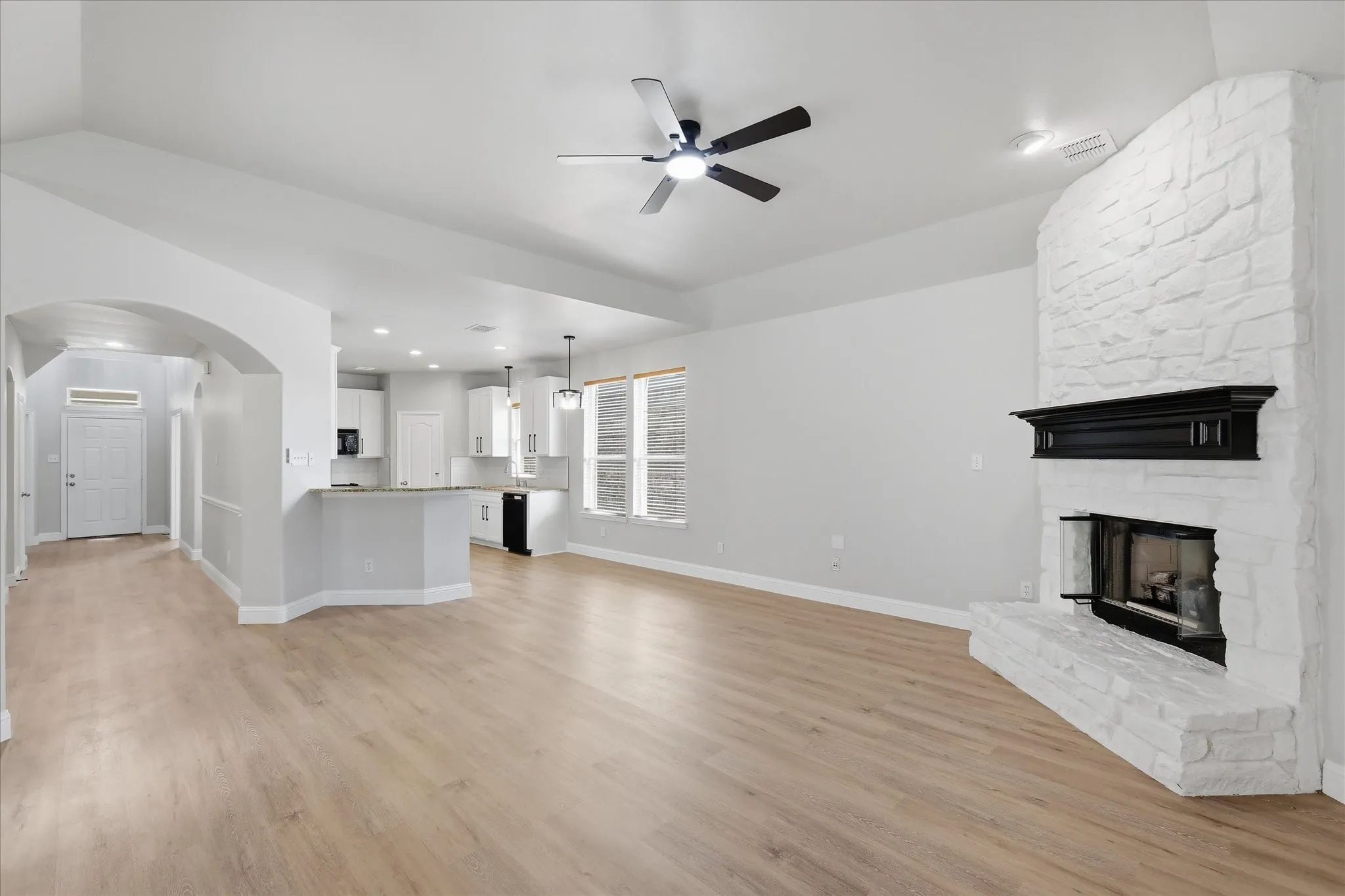 Living area featuring wood-finish flooring, a white brick fireplace with a black mantel, and a ceiling fan