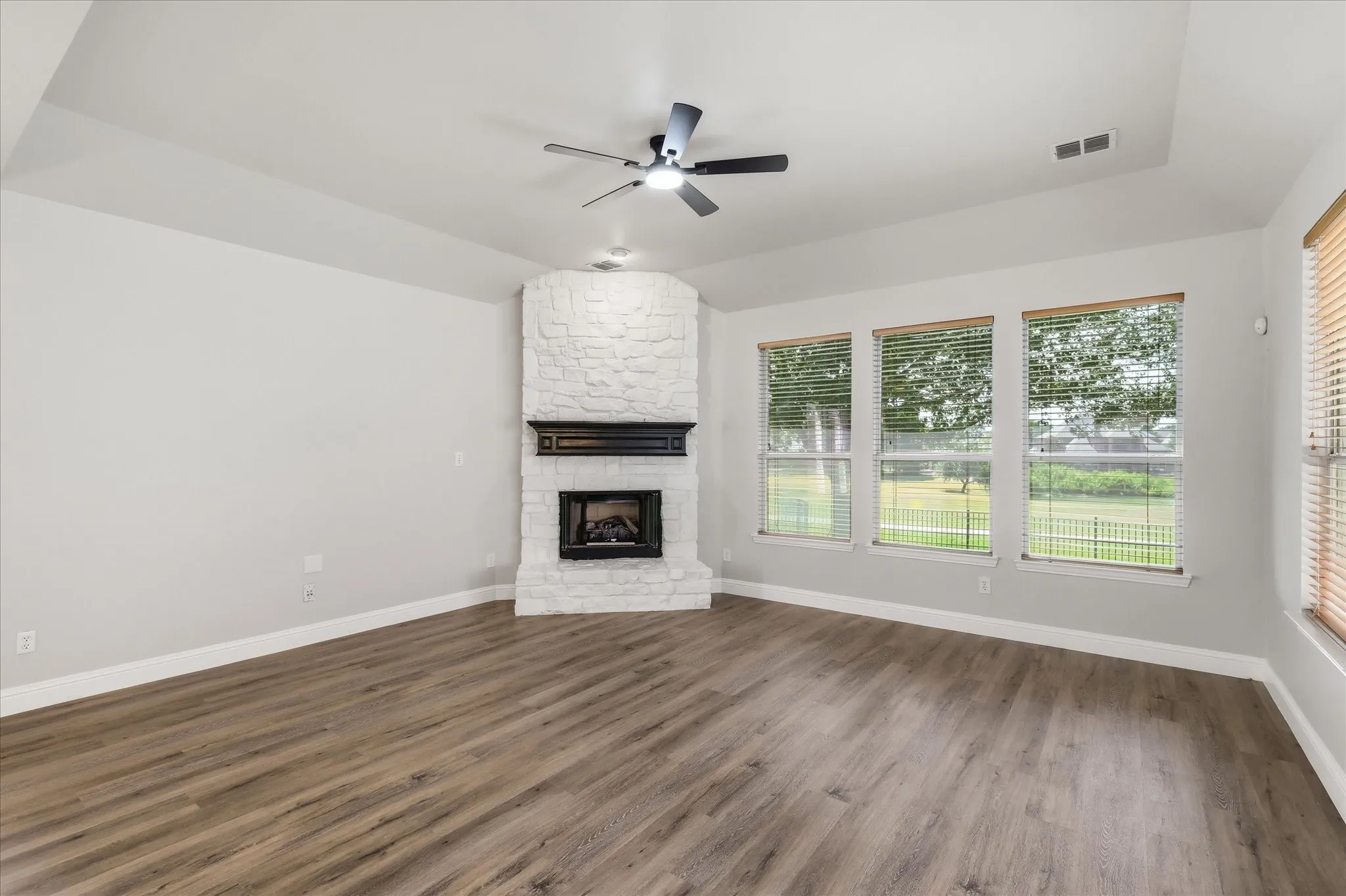 Vaulted ceiling with a ceiling fan, fireplace with a black mantel, wood-finish flooring, and multiple windows