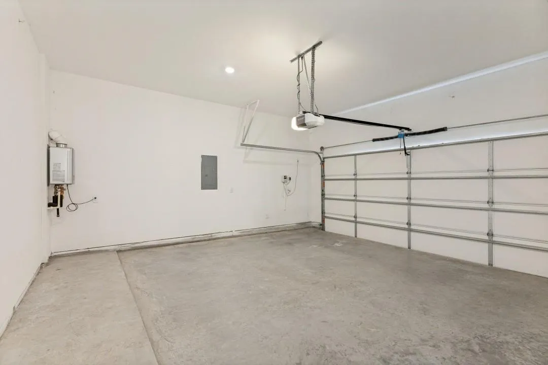 Spacious garage with a concrete floor, overhead lighting, an automatic garage door opener, and a wall-mounted water heater