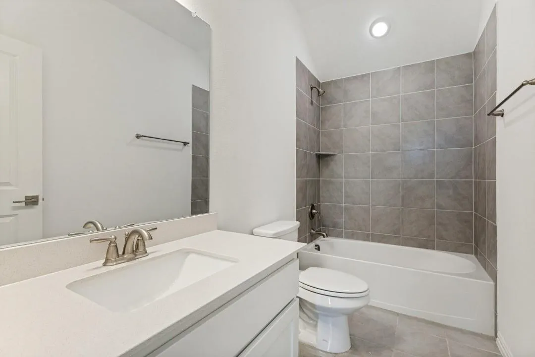 Modern bathroom featuring a white vanity with dual-sink configuration and brushed nickel faucetry, quartz countertop, large framed mirror, and a separate tile-surround shower-tub combination with chrome fixtures and recessed lighting