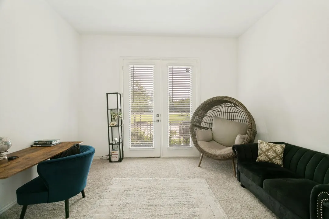 Bright, open living space featuring dual French doors with plantation shutters, neutral wood-finish flooring, and a sculptural hanging chair