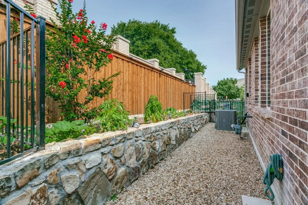 Brick exterior with a stone-faced retaining wall, gravel pathway, and privacy fencing