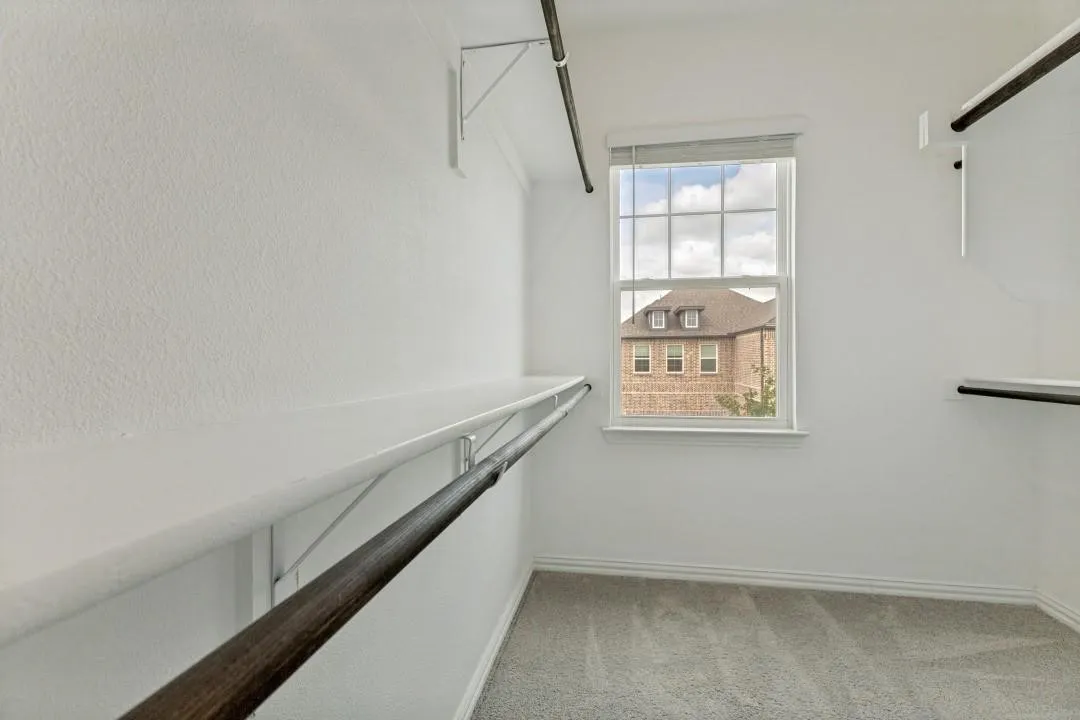 Built-in shelving and hanging rods, window with white blinds, and light-toned carpeting
