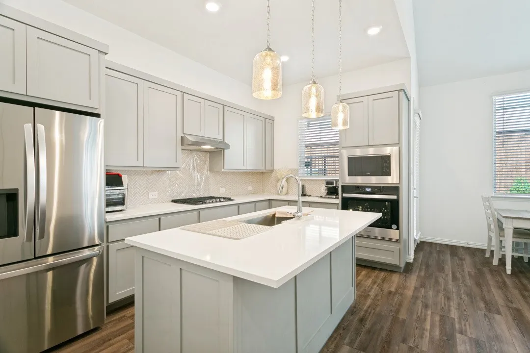 Kitchen featuring wood-finish flooring, light-toned cabinetry, stainless steel appliances, a center island with sink, and pendant lighting