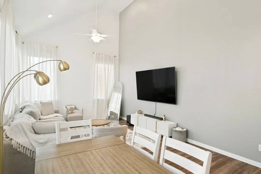 Bright, open bedroom featuring hardwood flooring, recessed ceiling lighting, wall-mounted flat-screen television with media console, and large mirror