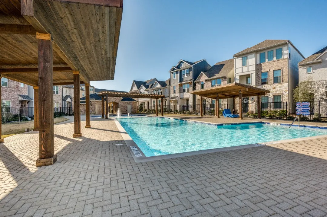 Resort-style resort pool with crystal-clear water, surrounded by herringbone-pattern paver decking and wooden pergola structures