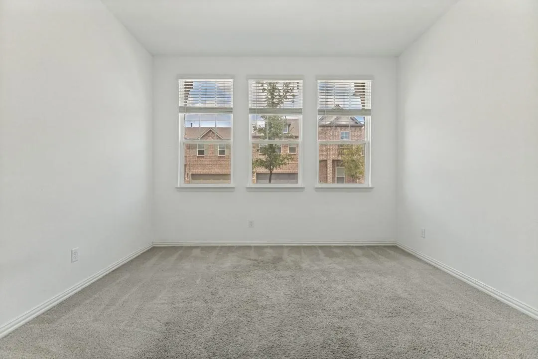 Three large windows with blinds, light gray wall-to-wall carpeting, and white painted walls