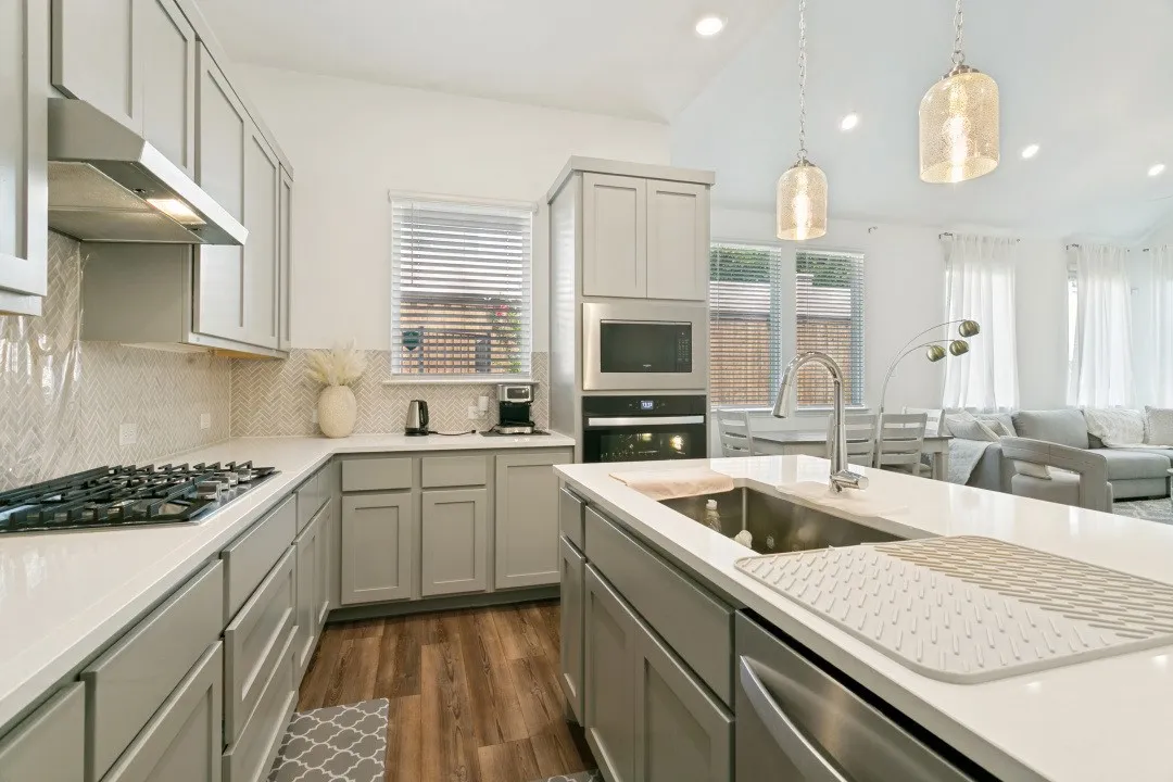 Chef's kitchen featuring custom cabinetry, gas cooktop, stainless steel appliances, and quartz countertops with waterfall island edge