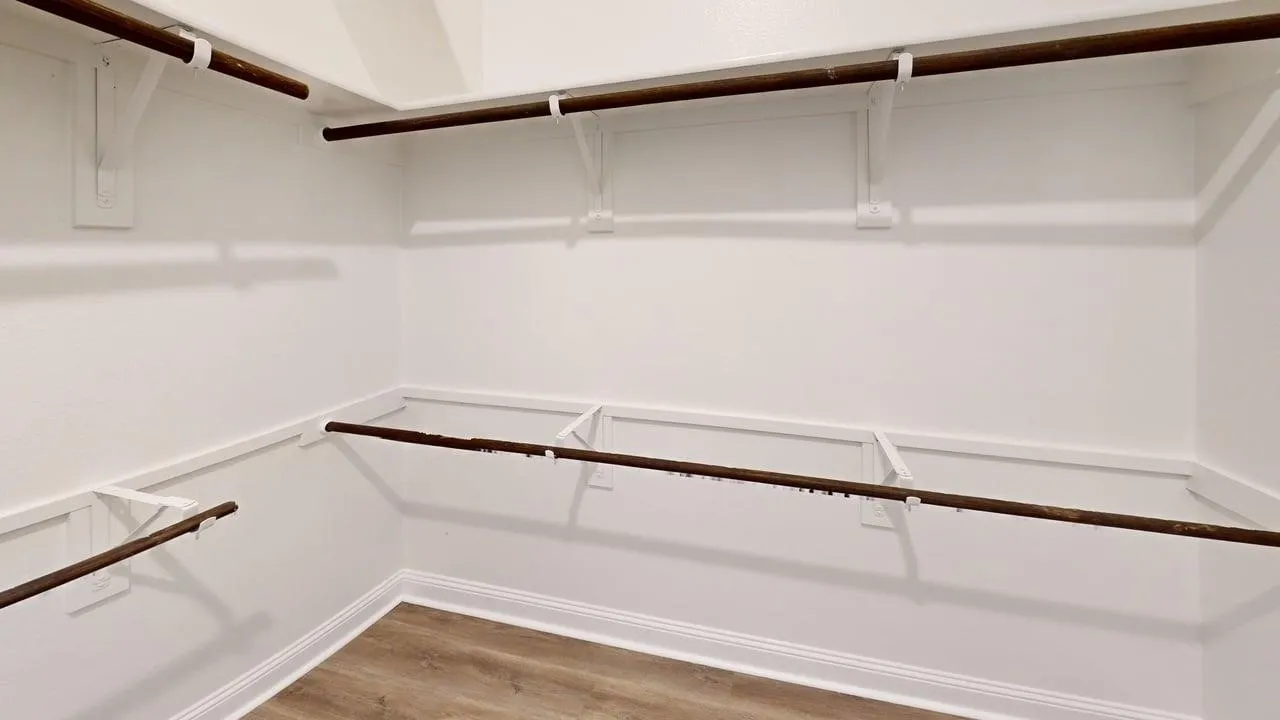 Walk-in closet with multiple hanging rods, built-in shelving, and wood-finish flooring