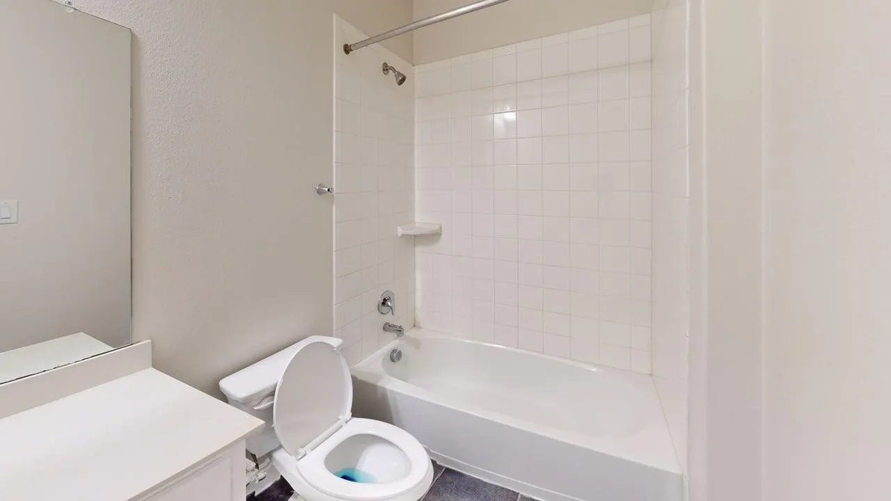 White tiled tub/shower combination, white vanity with integrated sink, and large wall-mounted mirror