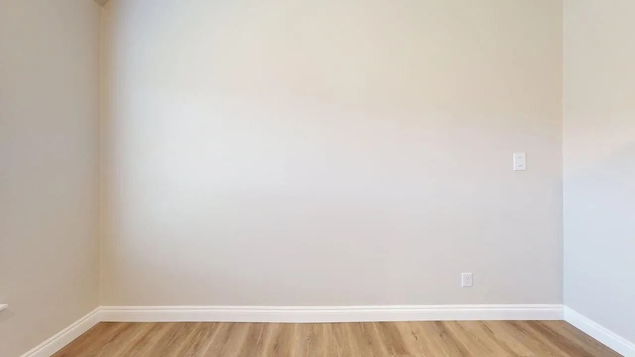 Wood-finish flooring with white trim, light-toned walls, and a wall-mounted light switch