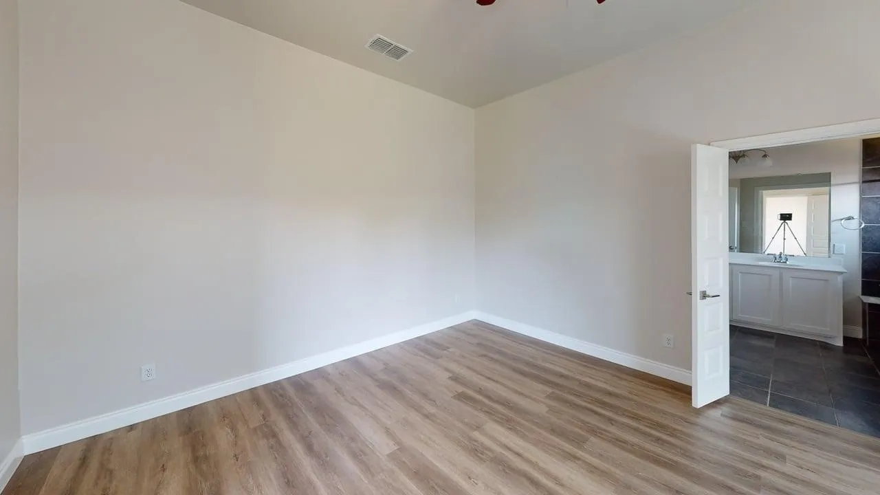 Wood-finish flooring, white trim, light-toned walls, and an open doorway to a bathroom with tile flooring and a vanity